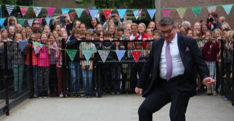 Onder luide aanmoediging van wel 300 kinderen legt wethouder Luca de bal voorzichtig voor zijn rechtervoet